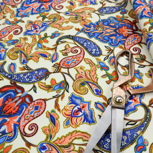 Cream-coloured fabric with an ornate repeating paisley pattern showcasing royal blue tear-drop motifs, vibrant coral and orange florals, and flowing leafy vines.   