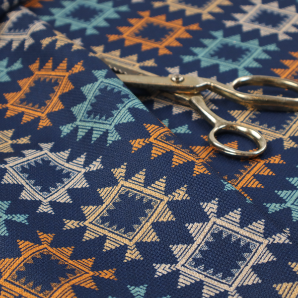 This fabric features repeated geometric shapes in blues, oranges and pinks on a navy blue background.