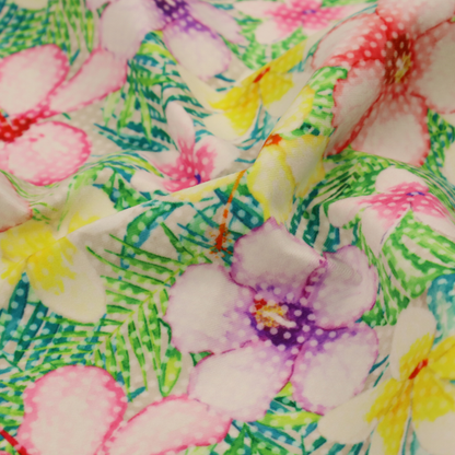 A vibrant tropical fabric pattern featuring pink and purple hibiscus flowers, yellow plumeria, and green palm leaves on a light grey dotted background.