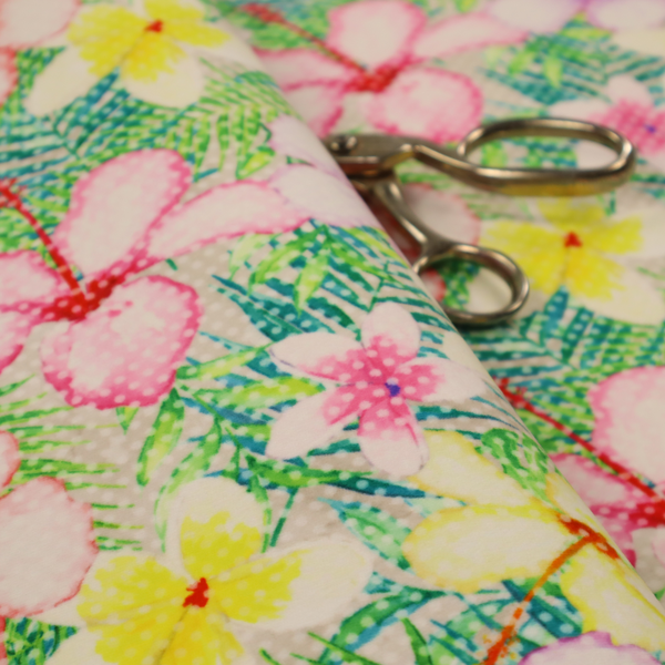 A vibrant tropical fabric pattern featuring pink and purple hibiscus flowers, yellow plumeria, and green palm leaves on a light grey dotted background.
