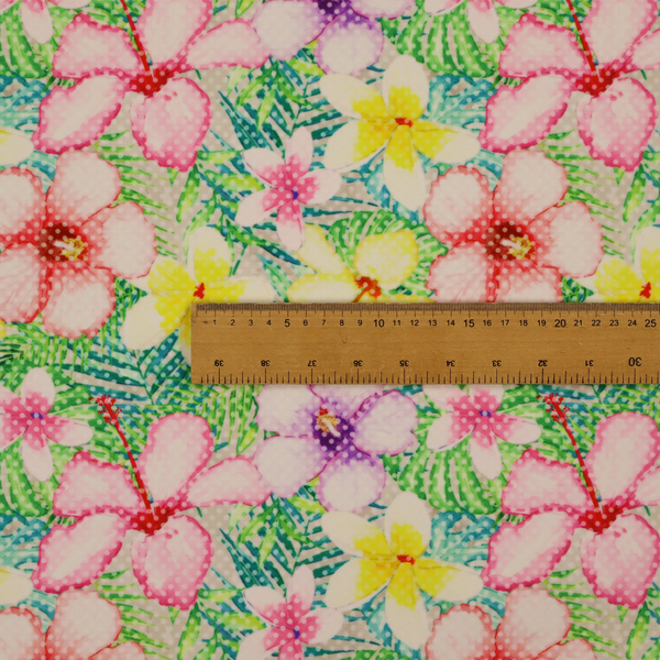 A vibrant tropical fabric pattern featuring pink and purple hibiscus flowers, yellow plumeria, and green palm leaves on a light grey dotted background.