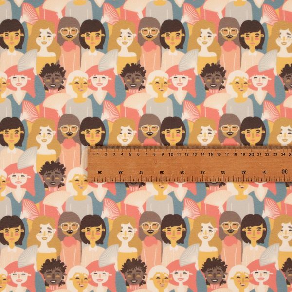 A whimsical, repeating fabric pattern featuring illustrated portraits of women with diverse hairstyles and accessories, some holding white hand fans, set against a warm coral-pink background.