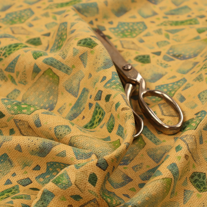An earthy, abstract fabric pattern featuring organic mosaic shapes in moss green, teal, and slate grey on a textured mustard yellow background.