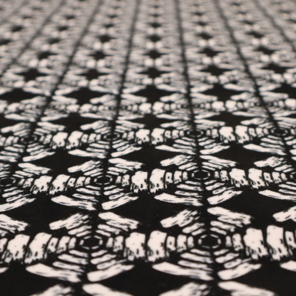 A bold, monochrome fabric pattern featuring a repeating hand-inked radial geometric design in cream on a solid black background.