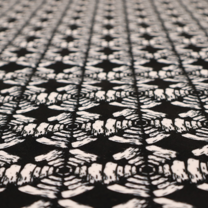 A bold, monochrome fabric pattern featuring a repeating hand-inked radial geometric design in cream on a solid black background.