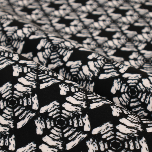 A bold, monochrome fabric pattern featuring a repeating hand-inked radial geometric design in cream on a solid black background.