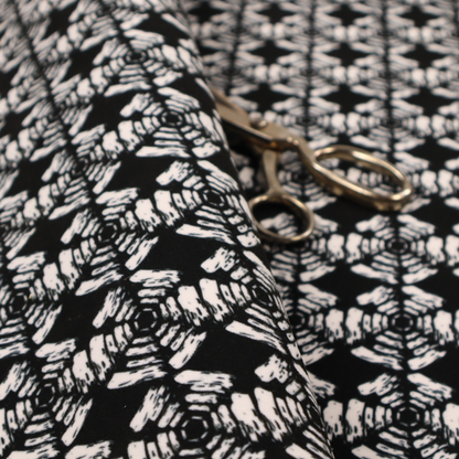 A bold, monochrome fabric pattern featuring a repeating hand-inked radial geometric design in cream on a solid black background.