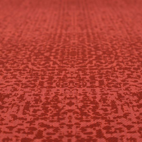 Distressed terracotta red fabric with a symmetrical, abstract medallion pattern and a weathered, block-print texture.