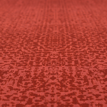 Distressed terracotta red fabric with a symmetrical, abstract medallion pattern and a weathered, block-print texture.