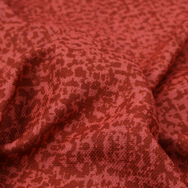 Distressed terracotta red fabric with a symmetrical, abstract medallion pattern and a weathered, block-print texture.
