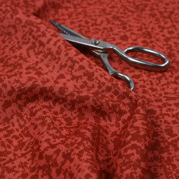 Distressed terracotta red fabric with a symmetrical, abstract medallion pattern and a weathered, block-print texture.