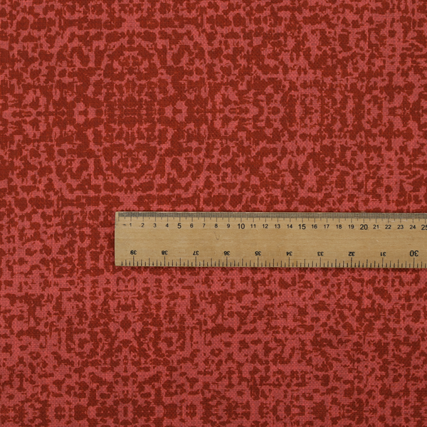 Distressed terracotta red fabric with a symmetrical, abstract medallion pattern and a weathered, block-print texture.