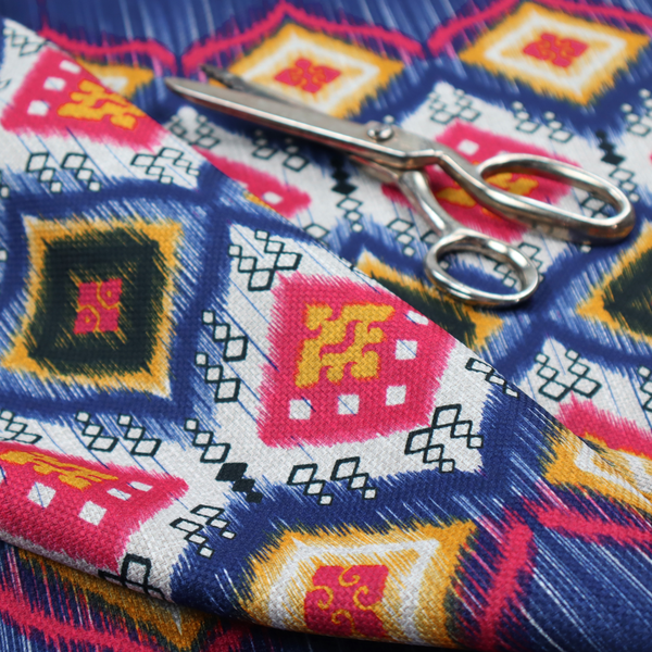 A high-energy textile with a large-scale geometric Ikat design. The pattern showcases concentric diamonds with feathered, "blurred" edges in electric blue, bright pink, and yellow, set against a background with vertical white striations.