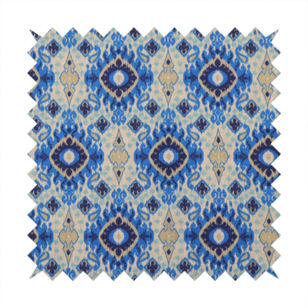 A repeating textile pattern featuring ornate blue Ikat medallions with a feathered, hand-painted appearance. The design includes smaller navy diamonds and sandy beige geometric shapes set against a light oatmeal-coloured fabric texture.