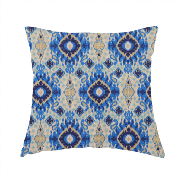 The fabric used to create this handmade cushion is a repeating textile pattern featuring ornate blue Ikat medallions with a feathered, hand-painted appearance. The design includes smaller navy diamonds and sandy beige geometric shapes set against a light oatmeal-coloured fabric texture.