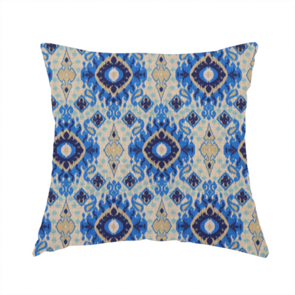 The fabric used to create this handmade cushion is a repeating textile pattern featuring ornate blue Ikat medallions with a feathered, hand-painted appearance. The design includes smaller navy diamonds and sandy beige geometric shapes set against a light oatmeal-coloured fabric texture.
