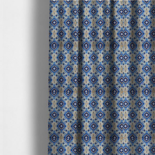 The fabric used to create these made-to-measure curtains is a repeating textile pattern featuring ornate blue Ikat medallions with a feathered, hand-painted appearance. The design includes smaller navy diamonds and sandy beige geometric shapes set against a light oatmeal-coloured fabric texture.