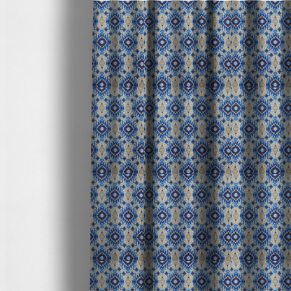 The fabric used to create these made-to-measure curtains is a repeating textile pattern featuring ornate blue Ikat medallions with a feathered, hand-painted appearance. The design includes smaller navy diamonds and sandy beige geometric shapes set against a light oatmeal-coloured fabric texture.