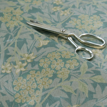 Muted green textile print with a complex, repeating botanical motif. The design features tightly packed five-petal flower clusters and delicate willow-like leaves in shades of dusty sage, teal, and pale lime green.