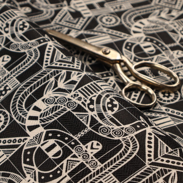 An intricate black and white repeating pattern featuring a grid of tribal-inspired geometric motifs. The design displays stylized, interlocking serpentine and curved forms filled with detailed line work, dots, and hatch marks. Circular gear-like symbols and triangular accents create a structured, rhythmic composition with a high-contrast, hand-drawn aesthetic on a textured fabric.