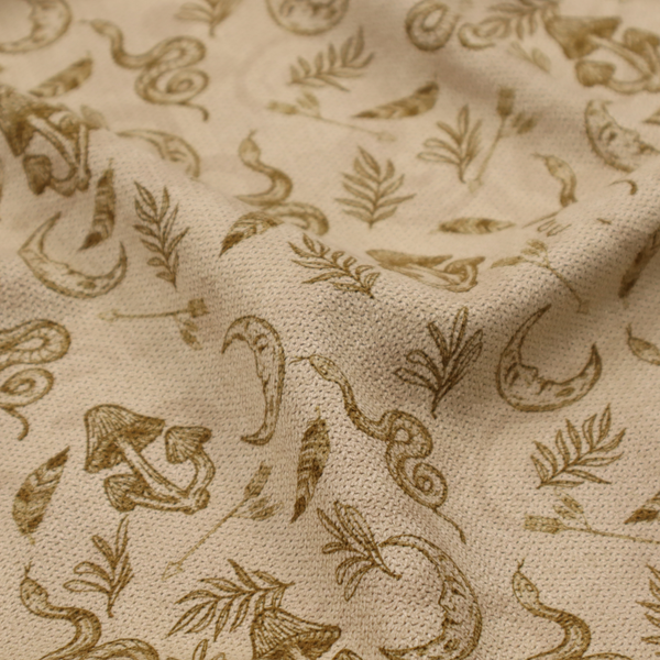 A light beige fabric featuring a repetitive boho-mystical pattern. The design is printed in a muted olive-brown ink and includes the following hand-drawn elements scattered across the material.