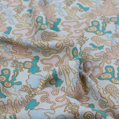 This fabric is a light blue fabric featuring a whimsical, abstract botanical pattern. The design is composed of organic, flowing shapes and illustrations in a pastel and jewel-tone palette.