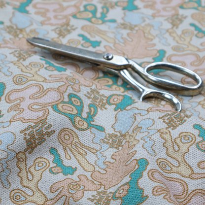 This fabric is a light blue fabric featuring a whimsical, abstract botanical pattern. The design is composed of organic, flowing shapes and illustrations in a pastel and jewel-tone palette.