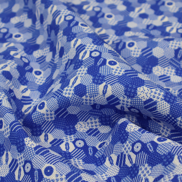 A detailed geometric fabric featuring a dense honeycomb or hexagonal patchwork pattern in blue and white.