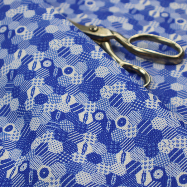 A detailed geometric fabric featuring a dense honeycomb or hexagonal patchwork pattern in blue and white.