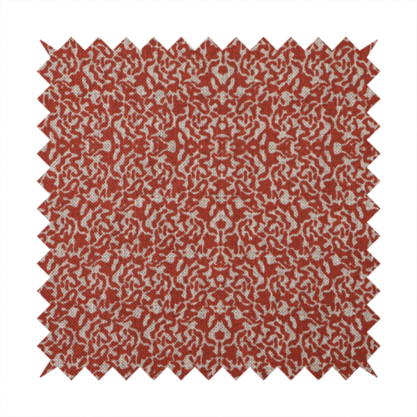 A decorative textile featuring a symmetrical, kaleidoscopic pattern in red and beige. The intricate, interlocking organic shapes create a dense, filigree-like design with a slightly weathered or distressed look. The fabric has a visible, fine-textured weave that gives the pattern a soft, matte appearance.