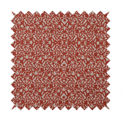A decorative textile featuring a symmetrical, kaleidoscopic pattern in red and beige. The intricate, interlocking organic shapes create a dense, filigree-like design with a slightly weathered or distressed look. The fabric has a visible, fine-textured weave that gives the pattern a soft, matte appearance.