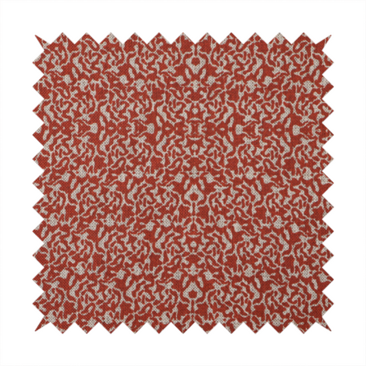 A decorative textile featuring a symmetrical, kaleidoscopic pattern in red and beige. The intricate, interlocking organic shapes create a dense, filigree-like design with a slightly weathered or distressed look. The fabric has a visible, fine-textured weave that gives the pattern a soft, matte appearance.