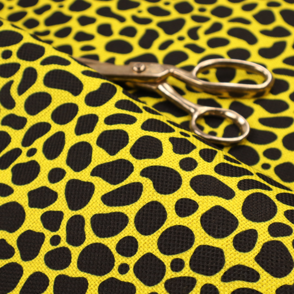 A bold cheetah-style animal print featuring irregular, black organic spots scattered across a bright canary yellow background.