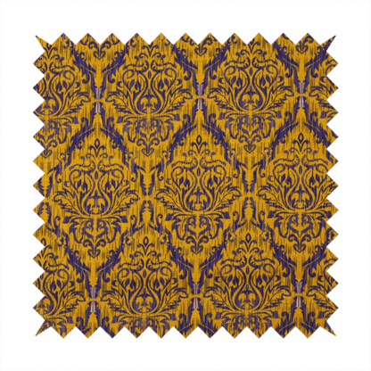 This fabric features a royal blue damask pattern layered over a deep mustard gold background. The design has an ikat-inspired finish, with vertical, feathered edges that give the ornate fleur-de-lis motifs a slightly blurred, textured appearance.