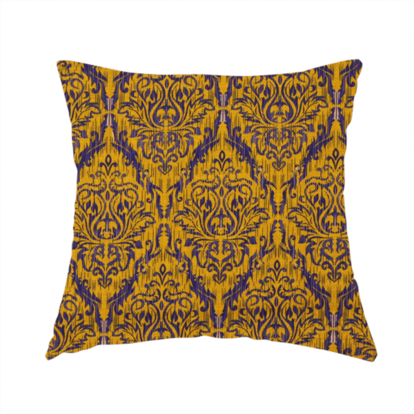 The fabric used to create this handmade cushion features a royal blue damask pattern layered over a deep mustard gold background. The design has an ikat-inspired finish, with vertical, feathered edges that give the ornate fleur-de-lis motifs a slightly blurred, textured appearance.