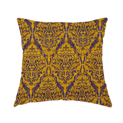 The fabric used to create this handmade cushion features a royal blue damask pattern layered over a deep mustard gold background. The design has an ikat-inspired finish, with vertical, feathered edges that give the ornate fleur-de-lis motifs a slightly blurred, textured appearance.