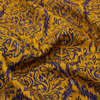 This fabric features a royal blue damask pattern layered over a deep mustard gold background. The design has an ikat-inspired finish, with vertical, feathered edges that give the ornate fleur-de-lis motifs a slightly blurred, textured appearance.