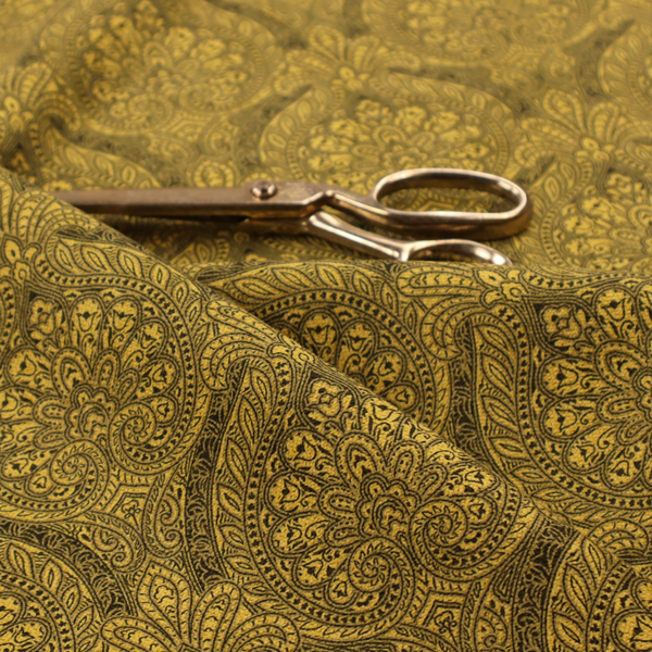 An intricate textile pattern featuring elaborate paisley-style medallions in black line work over an antique gold background. The design is highly detailed with swirling filigree, floral elements, and a repeating teardrop composition that creates a classic, traditional aesthetic.