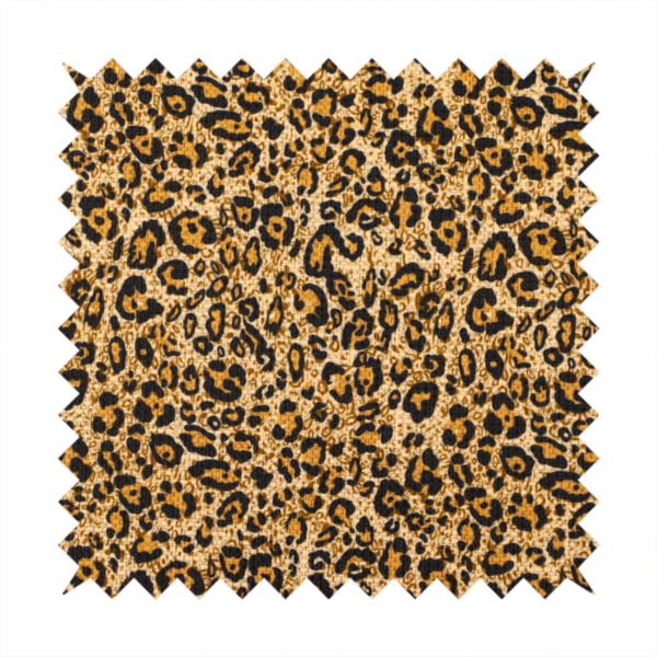 The design consists of irregular, organic black "rosette" shapes with golden-tan centres, set against a warm, sandy-beige background, creating a style of leopard print. The fabric has a visible textured, canvas-like weave, giving the pattern a slightly rugged and tactile appearance.