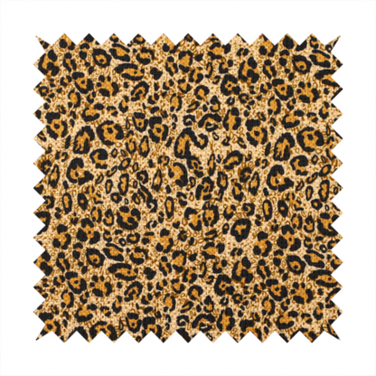 The design consists of irregular, organic black "rosette" shapes with golden-tan centres, set against a warm, sandy-beige background, creating a style of leopard print. The fabric has a visible textured, canvas-like weave, giving the pattern a slightly rugged and tactile appearance.
