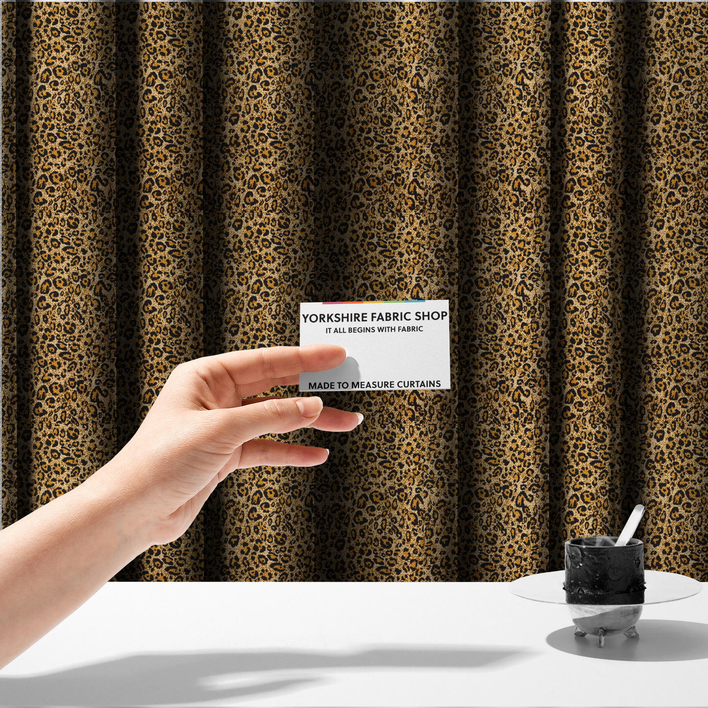 The fabric used to create these made-to-measure curtains consists of irregular, organic black "rosette" shapes with golden-tan centres, set against a warm, sandy-beige background, creating a style of leopard print. The fabric has a visible textured, canvas-like weave, giving the pattern a slightly rugged and tactile appearance.