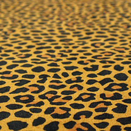 A high-contrast animal print fabric featuring a dense leopard-inspired pattern. The design consists of irregular black spots and open rosettes with warm orange-brown centres, set against a vibrant mustard-yellow background. The print is small-scale and tightly packed, with a visible fine-grained textile texture