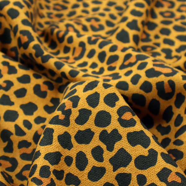 A high-contrast animal print fabric featuring a dense leopard-inspired pattern. The design consists of irregular black spots and open rosettes with warm orange-brown centres, set against a vibrant mustard-yellow background. The print is small-scale and tightly packed, with a visible fine-grained textile texture