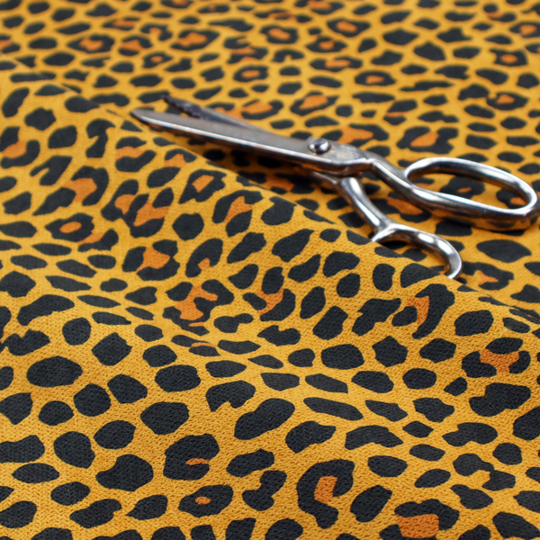 A high-contrast animal print fabric featuring a dense leopard-inspired pattern. The design consists of irregular black spots and open rosettes with warm orange-brown centres, set against a vibrant mustard-yellow background. The print is small-scale and tightly packed, with a visible fine-grained textile texture