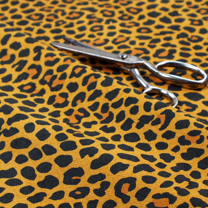 A high-contrast animal print fabric featuring a dense leopard-inspired pattern. The design consists of irregular black spots and open rosettes with warm orange-brown centres, set against a vibrant mustard-yellow background. The print is small-scale and tightly packed, with a visible fine-grained textile texture