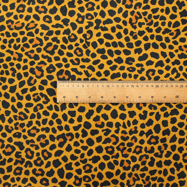 A high-contrast animal print fabric featuring a dense leopard-inspired pattern. The design consists of irregular black spots and open rosettes with warm orange-brown centres, set against a vibrant mustard-yellow background. The print is small-scale and tightly packed, with a visible fine-grained textile texture
