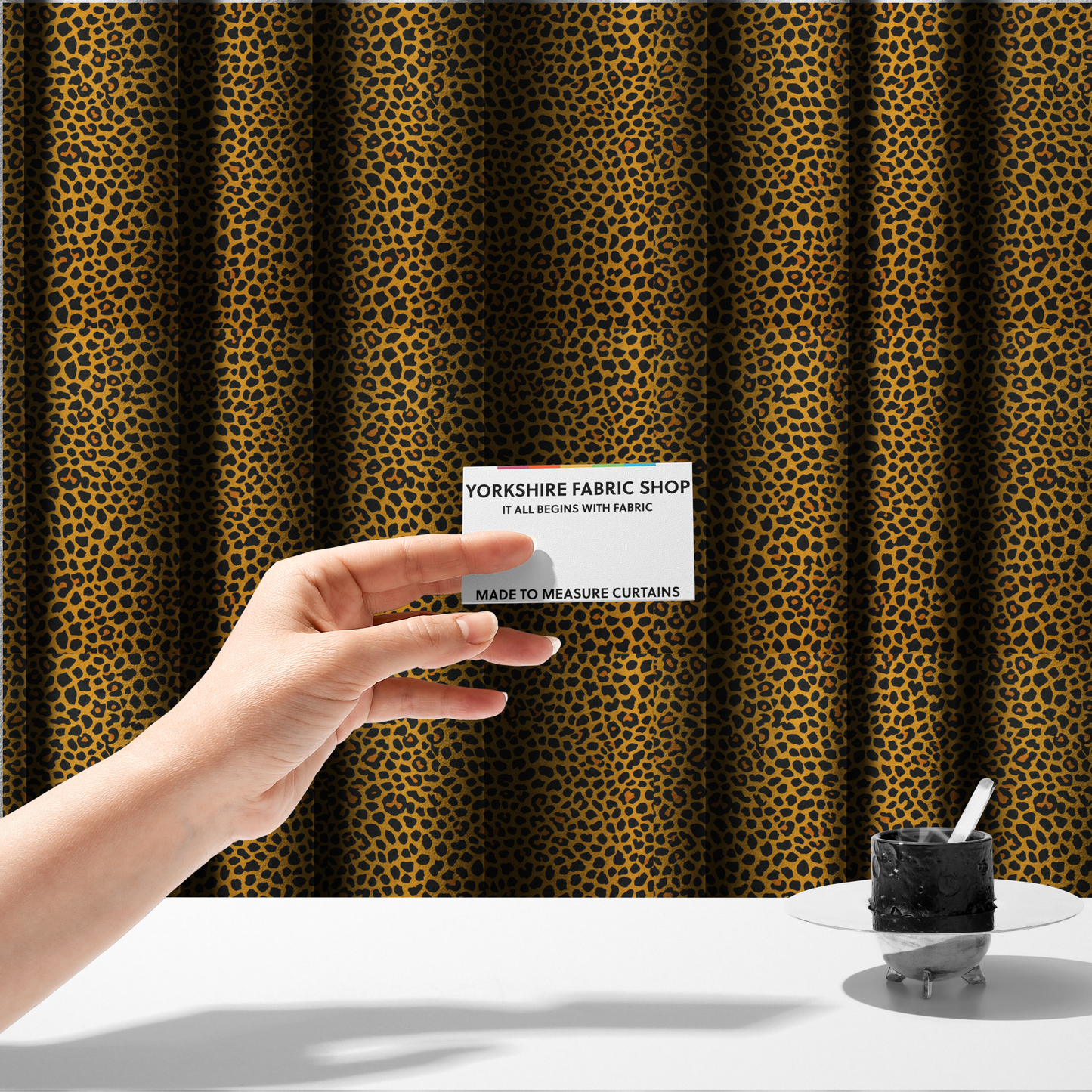 The fabric used to create these made-to-measure curtains is a high-contrast animal print fabric featuring a dense leopard-inspired pattern. The design consists of irregular black spots and open rosettes with warm orange-brown centres, set against a vibrant mustard-yellow background. The print is small-scale and tightly packed, with a visible fine-grained textile texture