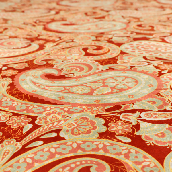 A vibrant, warm-toned textile featuring large-scale paisley teardrop motifs in shades of cream, pale mint, and soft orange against a bold red background. The intricate patterns within the paisley shapes include delicate floral borders and internal mandalas, surrounded by smaller scattered flower accents for a rich, traditional Indian-inspired aesthetic.