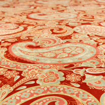 A vibrant, warm-toned textile featuring large-scale paisley teardrop motifs in shades of cream, pale mint, and soft orange against a bold red background. The intricate patterns within the paisley shapes include delicate floral borders and internal mandalas, surrounded by smaller scattered flower accents for a rich, traditional Indian-inspired aesthetic.