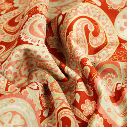 A vibrant, warm-toned textile featuring large-scale paisley teardrop motifs in shades of cream, pale mint, and soft orange against a bold red background. The intricate patterns within the paisley shapes include delicate floral borders and internal mandalas, surrounded by smaller scattered flower accents for a rich, traditional Indian-inspired aesthetic.